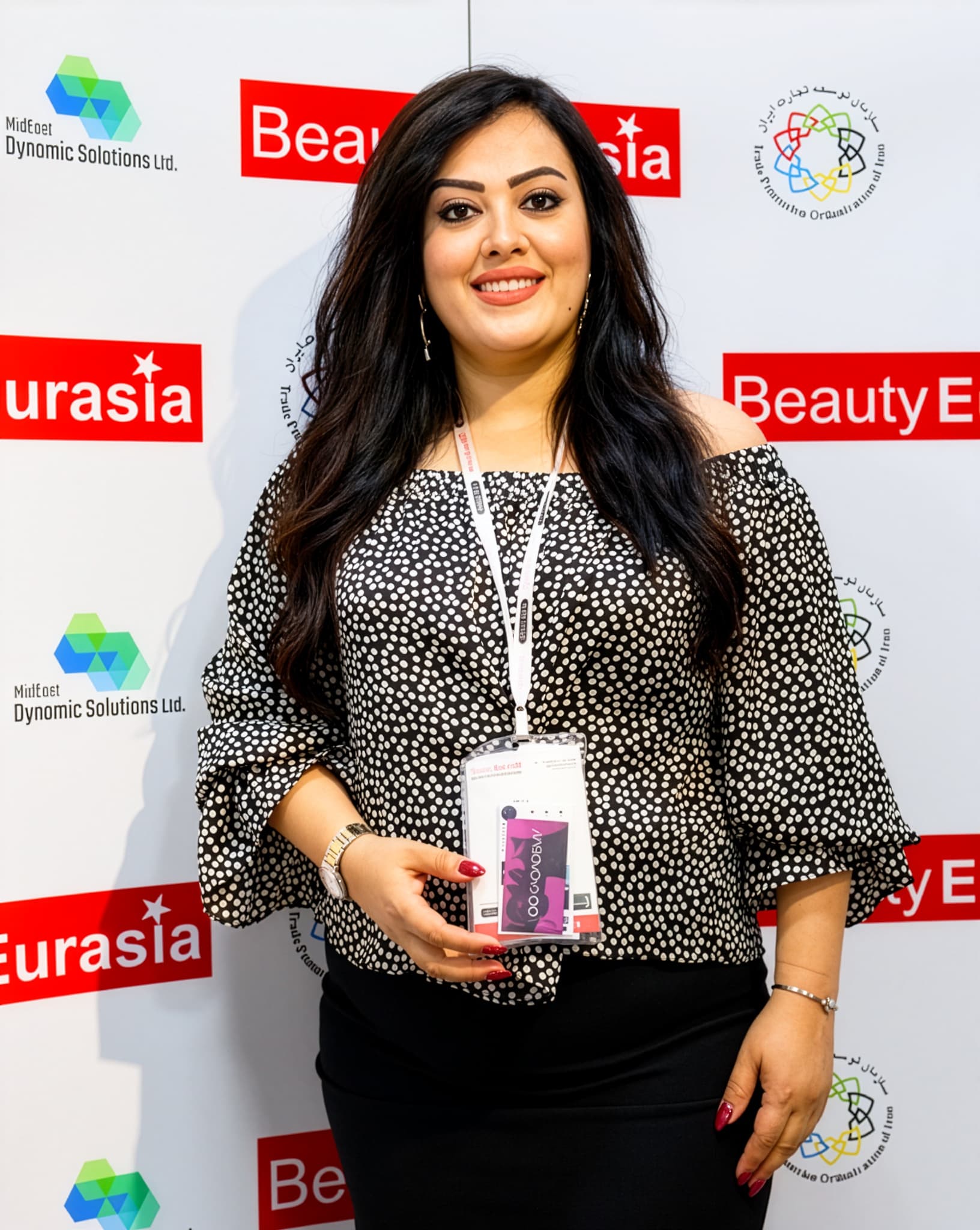 Sada Gholipour Beauty Eurasia fuarının basın duvarı önünde, boynunda katılımcı kartıyla
